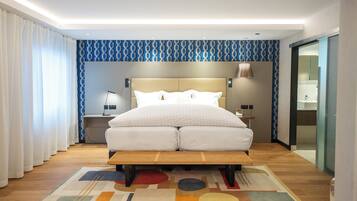 Une chambre d’hôtel moderne avec un grand lit, une table de chevet, une lampe et vue sur la salle de bain.