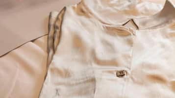 Une chemise de couleur claire, soigneusement pliée, est posée sur un lit dont le couvre-lit est à motifs floraux.