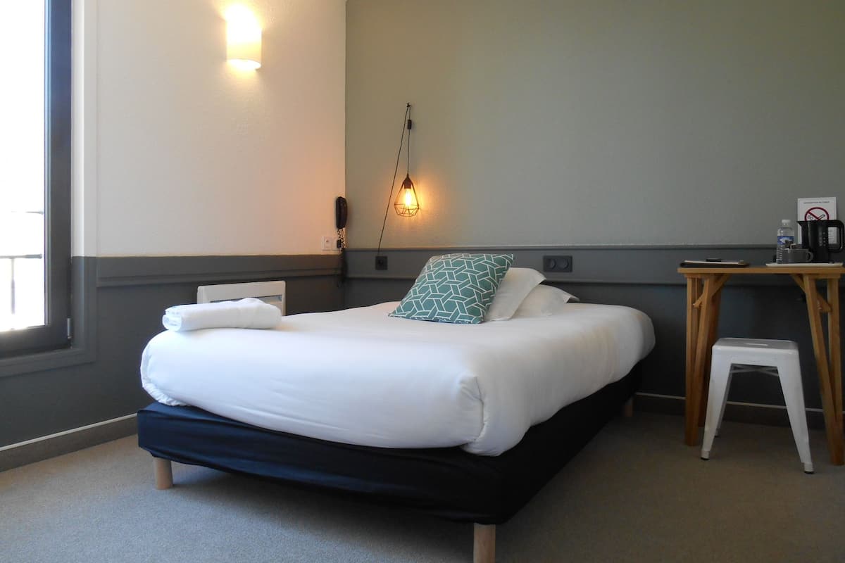 Een hotelkamer met een bed, nachtkastje en een bureau met stoel.