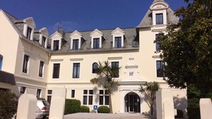 Un grand bâtiment historique à la façade symétrique, doté de nombreuses fenêtres et d’une entrée centrale.
