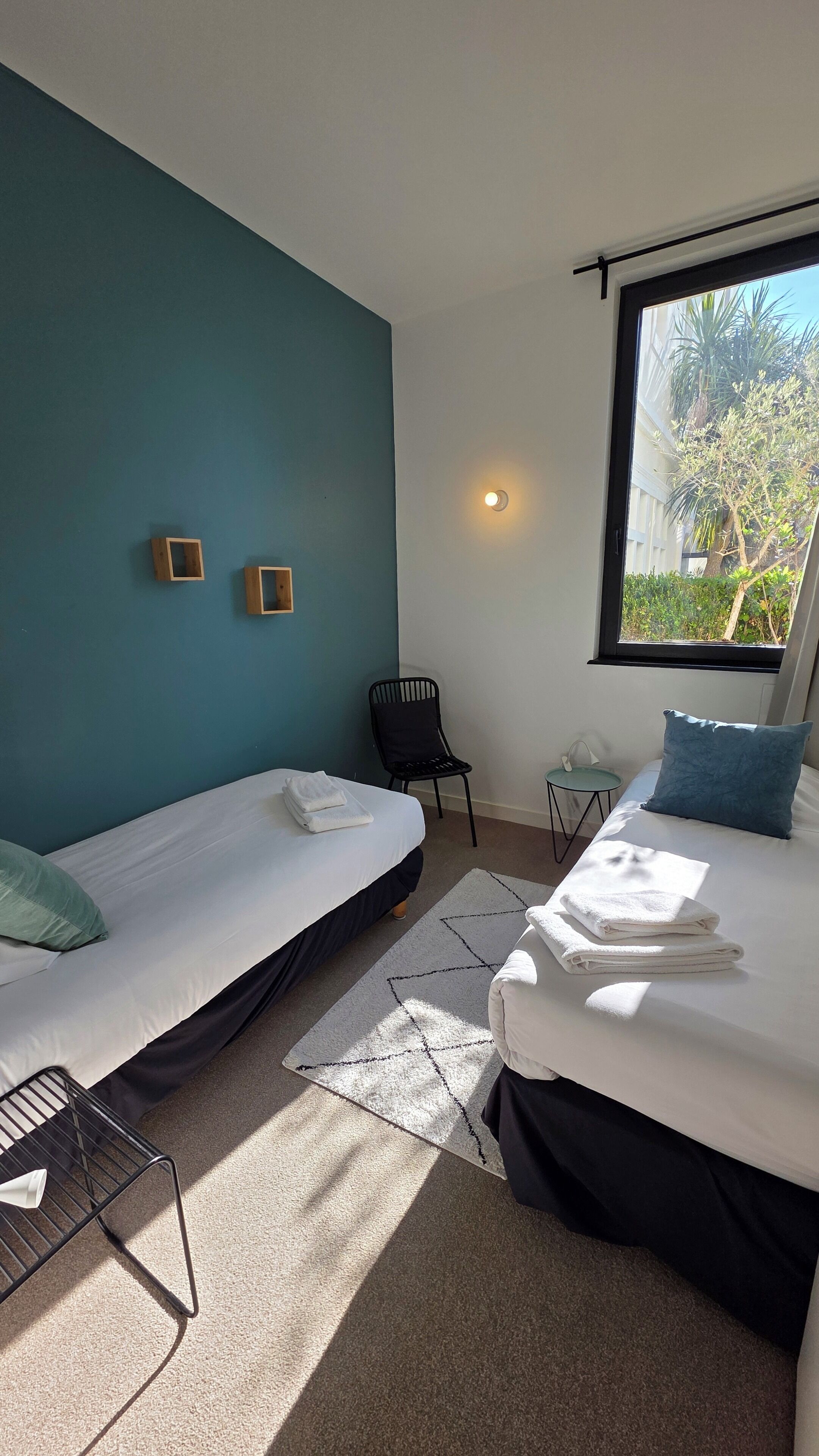 Une chambre avec deux lits, une chaise, une petite table et une fenêtre donnant sur un paysage verdoyant.