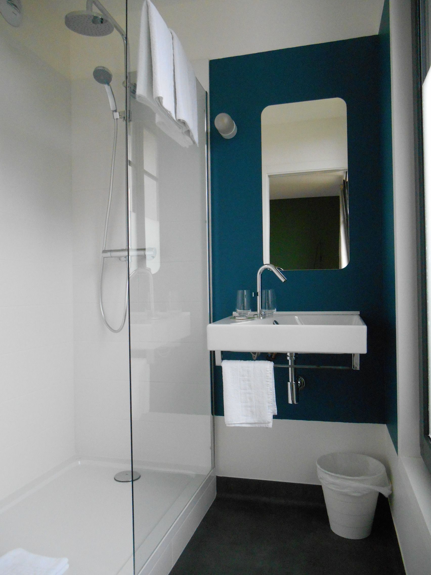 Ein modernes Badezimmer mit einer Duschkabine aus Glas, einem weißen Waschbecken mit Spiegel darüber und einer weißen Mülleiste.