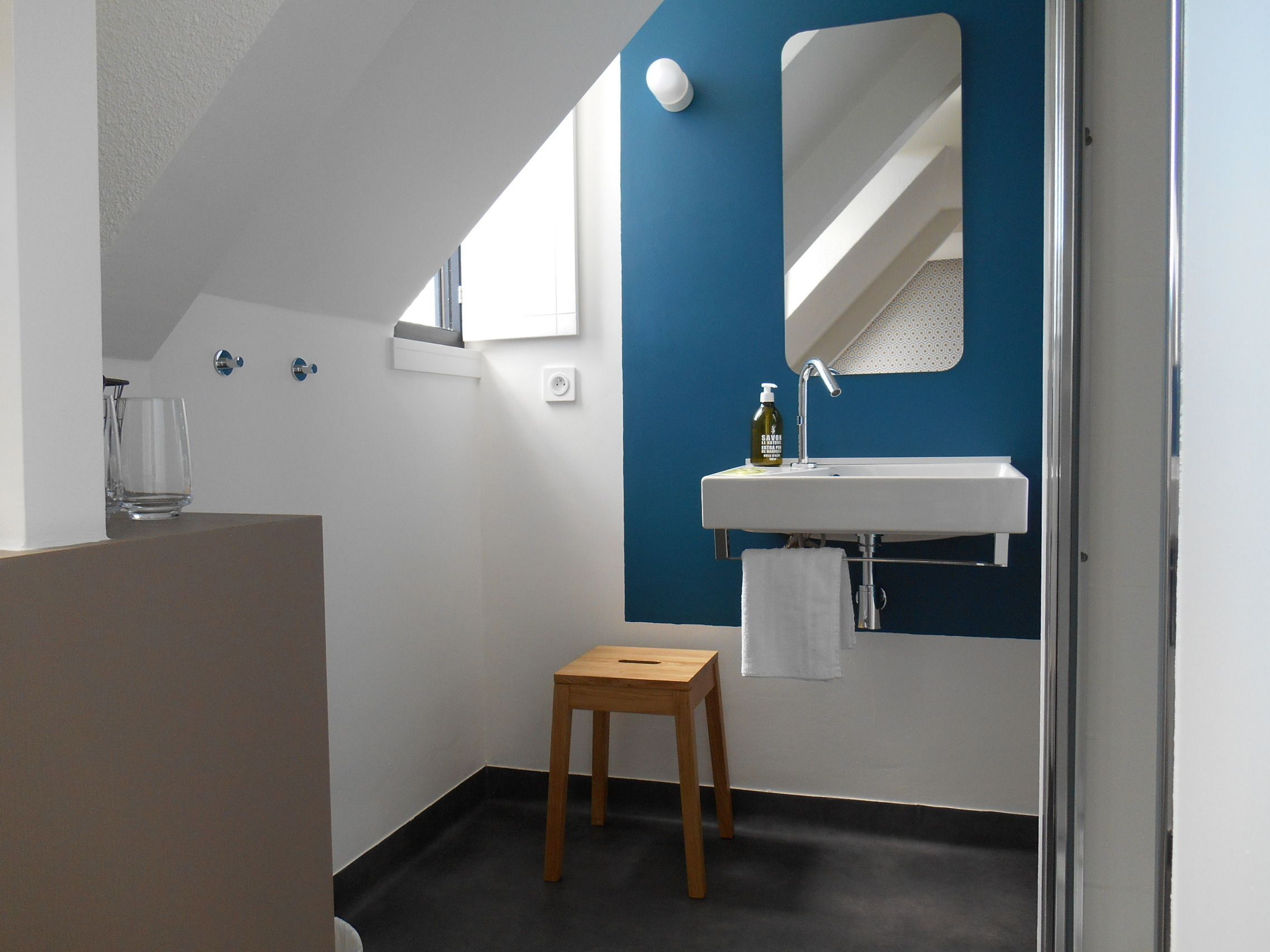 Un baño moderno con un lavamanos blanco, un espejo y un taburete de madera pequeño.