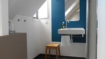 Un baño moderno con un lavamanos blanco, un espejo y un taburete de madera pequeño.