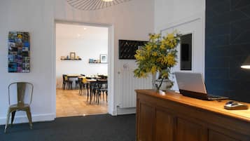 A reception area with a wooden desk, a laptop, a vase with yellow flowers, and a bulletin board with various items.