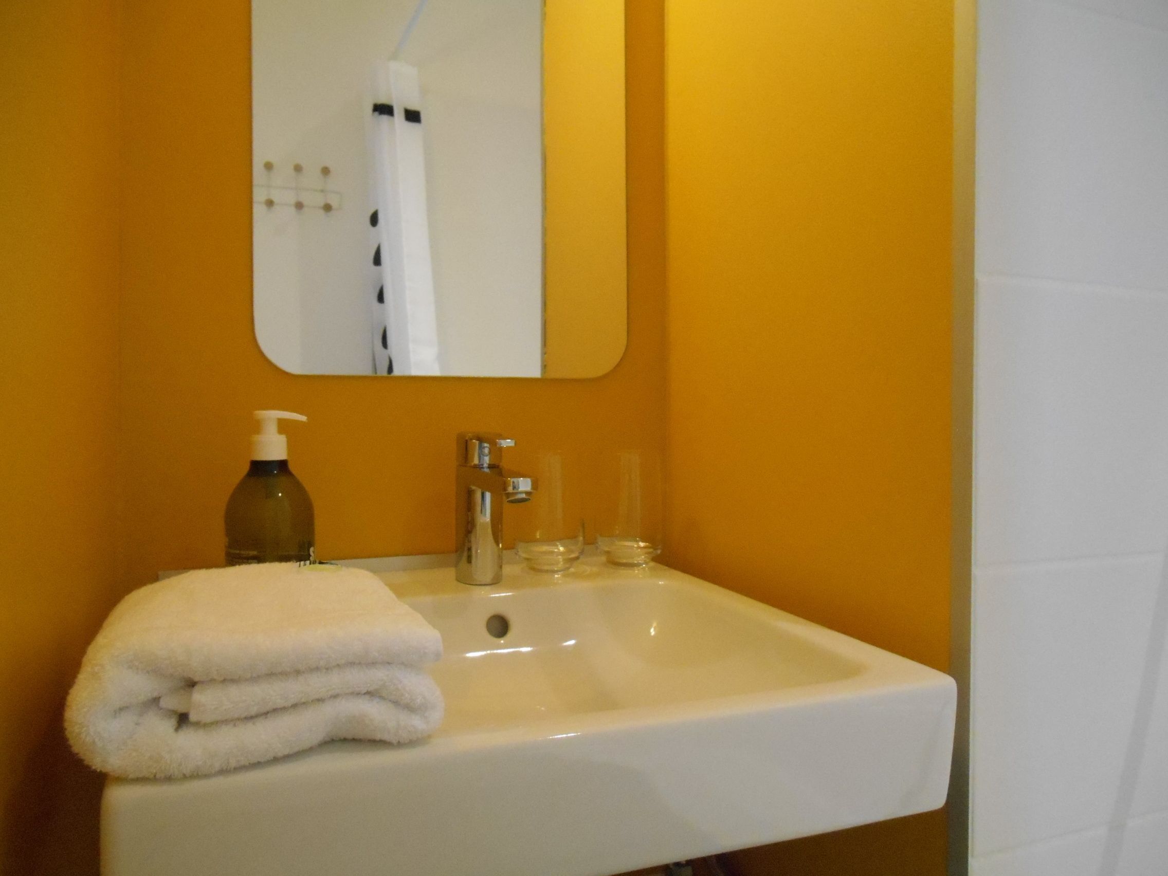 A bathroom with a white sink, a mirror, a bottle of soap, and a towel.