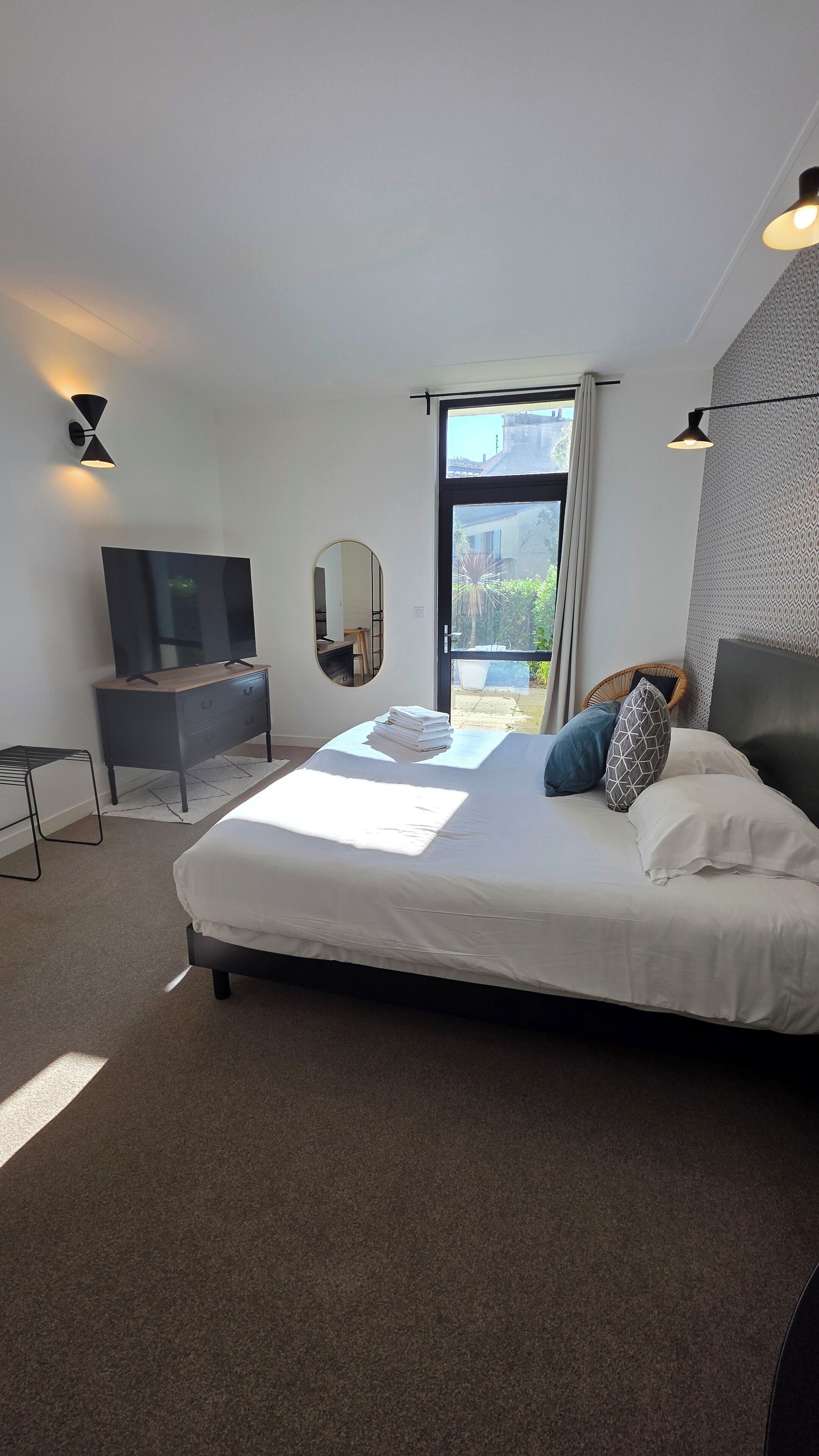 A modern bedroom with a large bed, a TV, a dresser, and a balcony view.