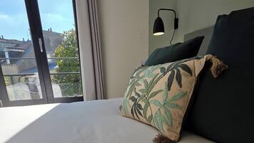 A neatly made bed with a green booklet on it, a dark green pillow, and a black lamp on the wall.