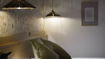 A bedroom with a bed, two pillows, a headboard, a wall with a framed picture, and two pendant lights.