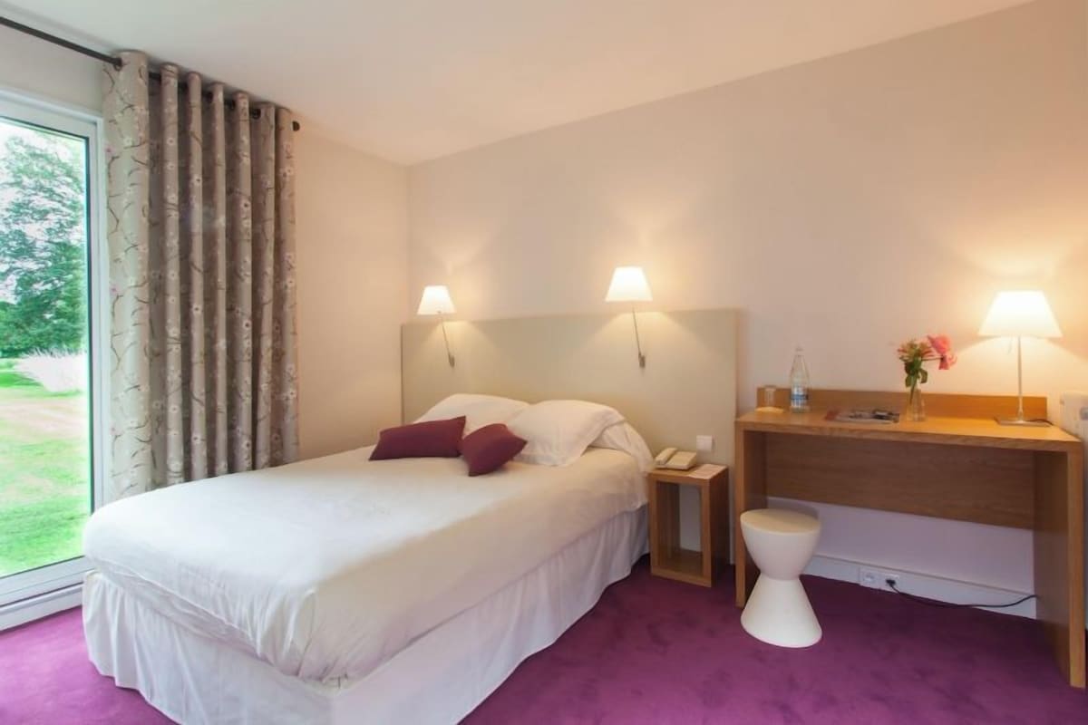 A hotel room with a bed, bedside lamps, a desk, and a toilet.