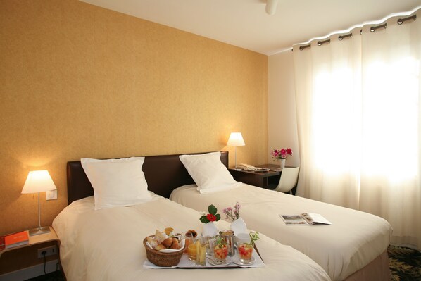 Une chambre d’hôtel avec deux lits, une table de chevet avec une lampe, une petite table de nuit avec un téléphone et un plateau de petit-déjeuner posé sur les lits.