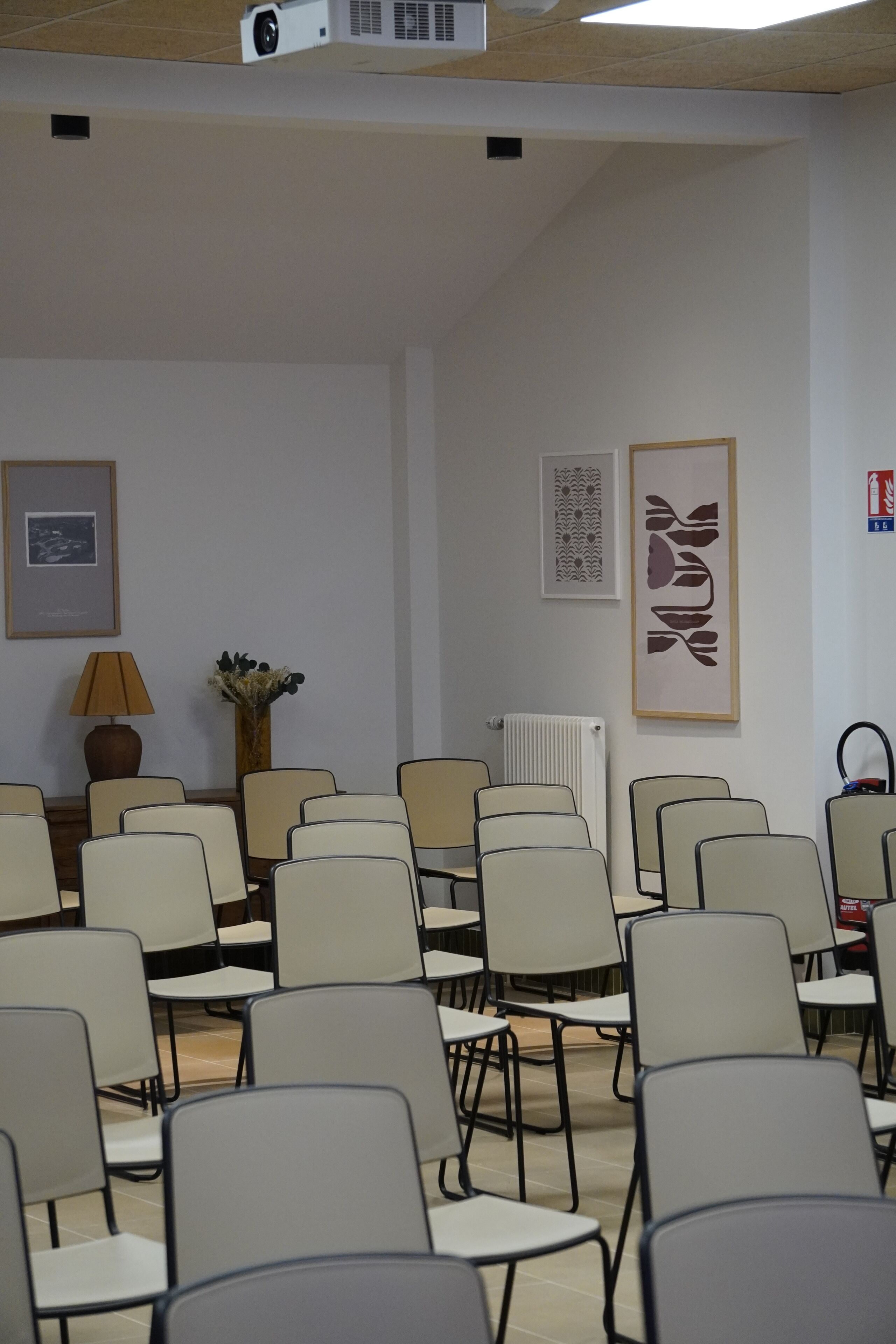 A conference room with rows of chairs, a projector, a lamp, and framed artwork on the walls.