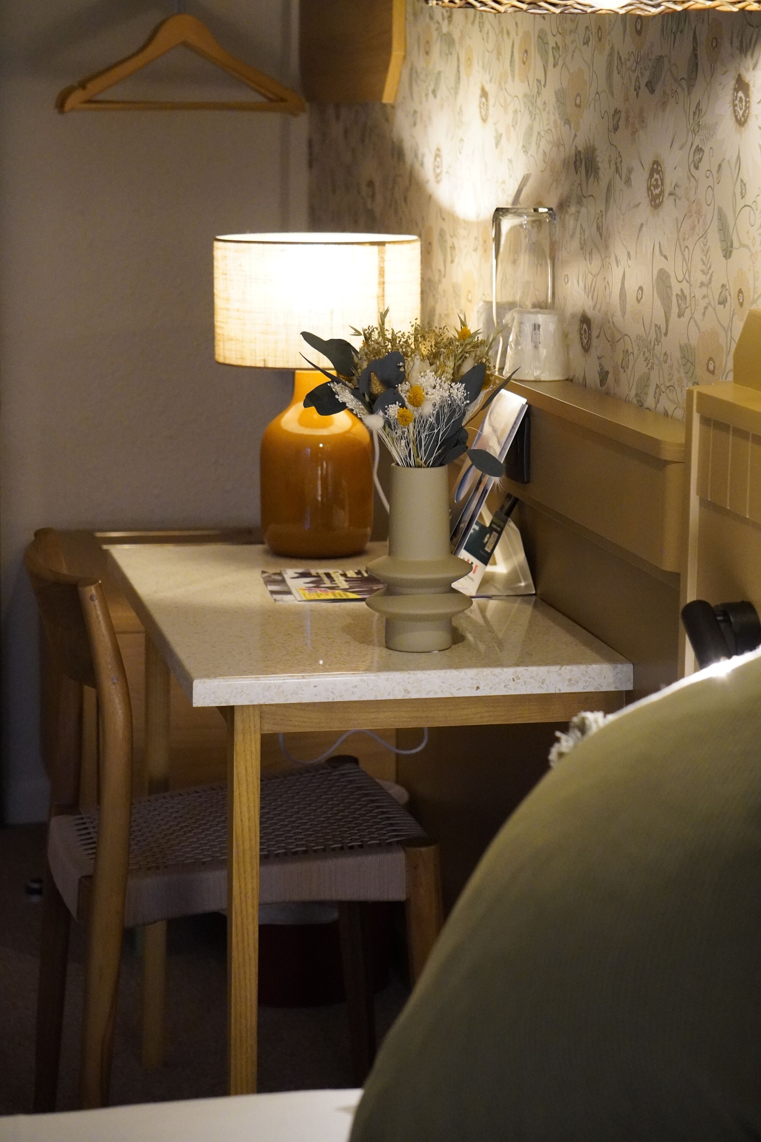 A small table with a lamp, a vase with flowers, and a magazine holder.