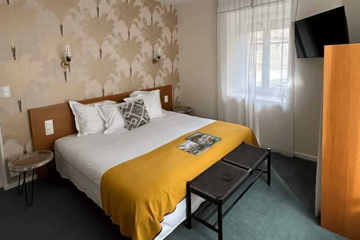 Una habitación de hotel con una cama, un banco, un televisor y un armario de madera.