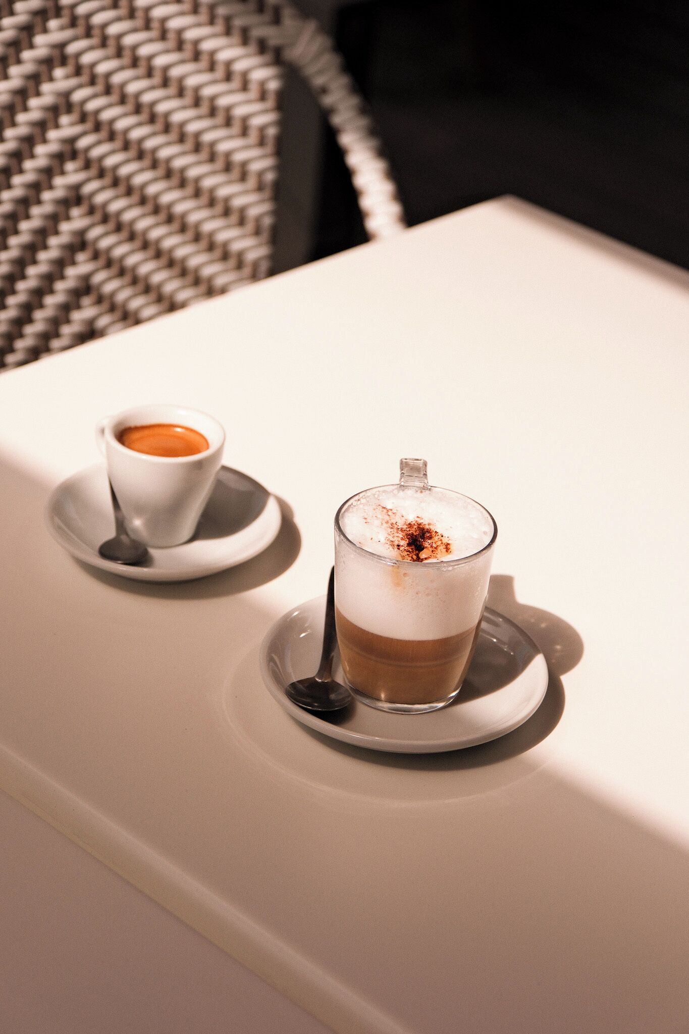 Dos tazas de café sobre una mesa, con una silla tejida al fondo.