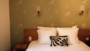A hotel room with a bed, pillows, a nightstand, and wall sconces. - Hotel de la Vallee (Dinard)