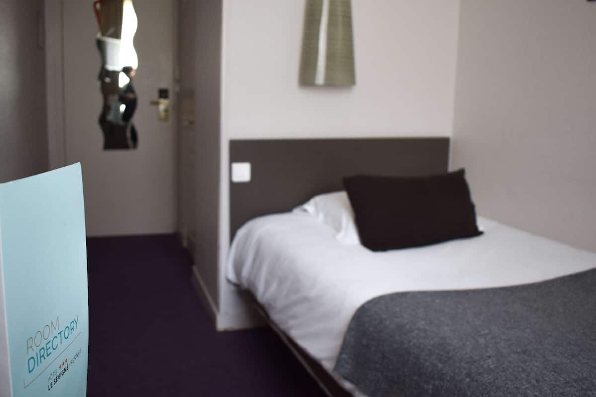 A hotel room with a bed, a bedside table, a wall-mounted mirror, and a door.