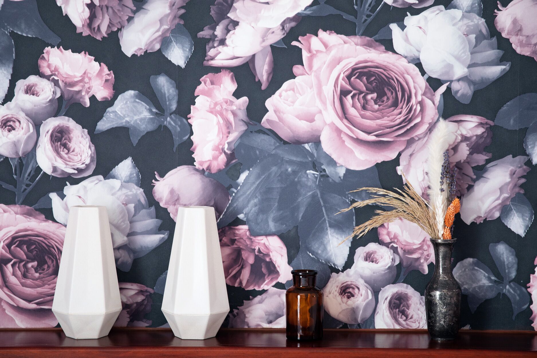 Una repisa con tres jarrones sobre un fondo de papel tapiz floral.