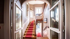 Un escalier recouvert d’une moquette rouge, avec des marches en bois et une porte en verre en haut.