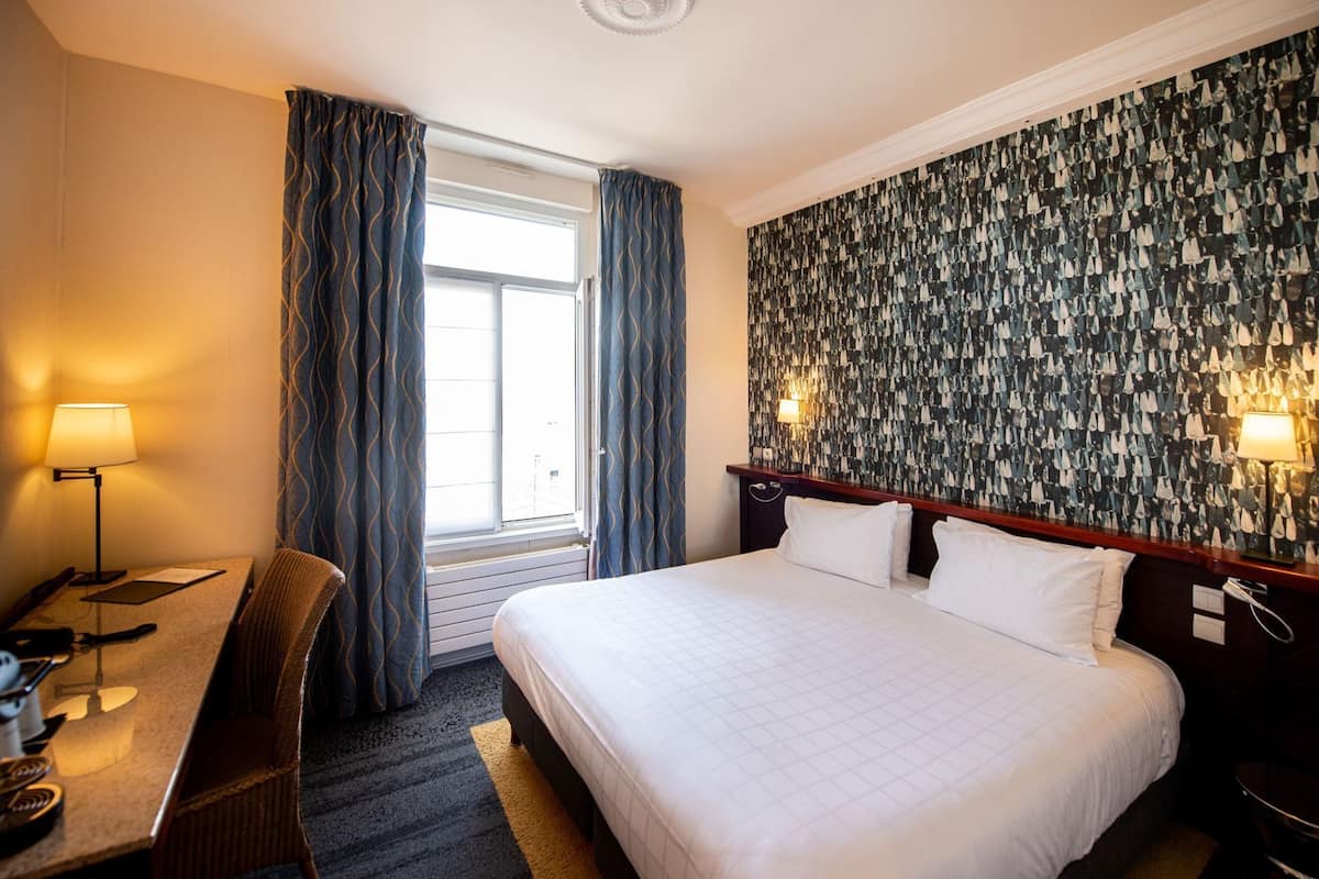 Een hotelkamer met een bed, bureau, stoel en behang met een patroon.