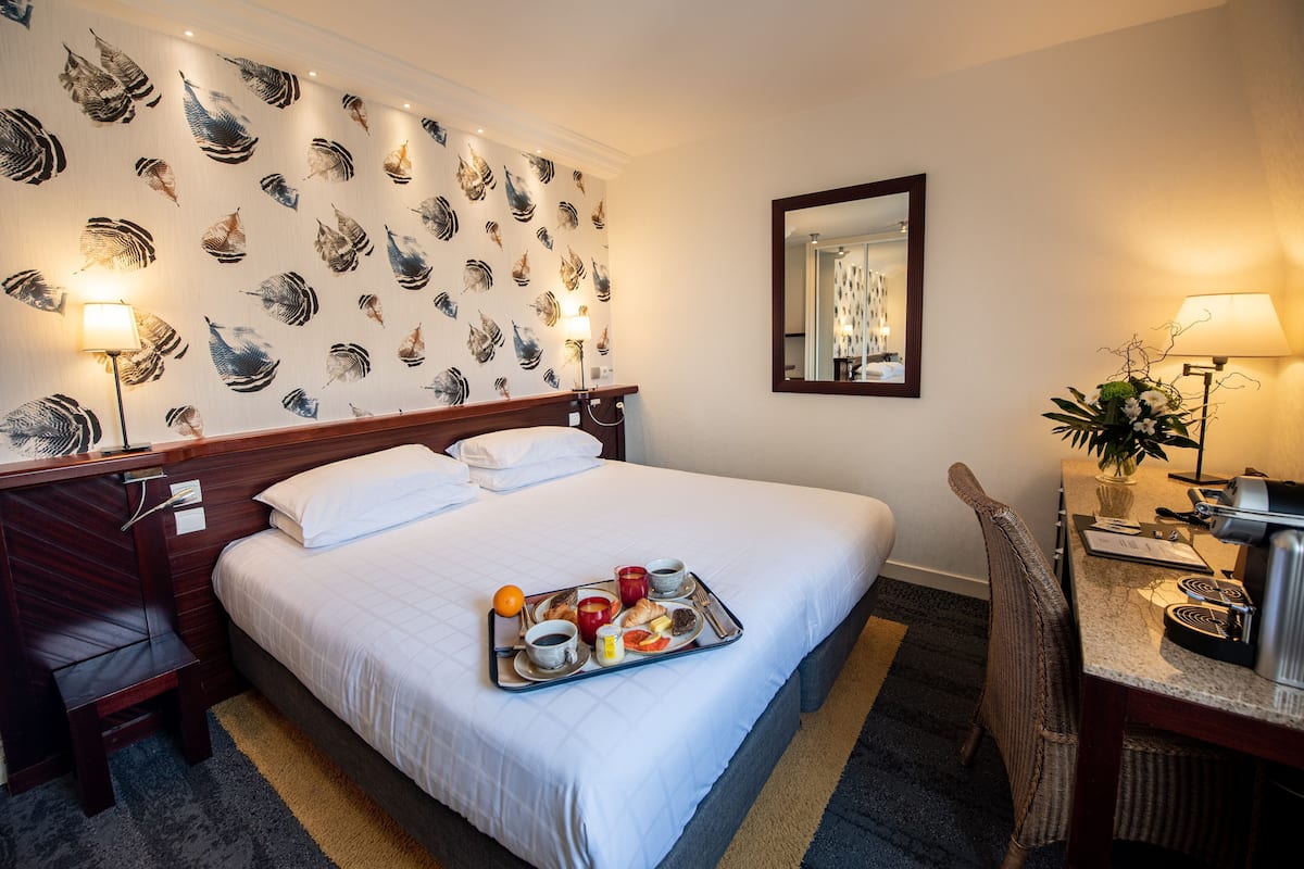 Hotelkamer met een bed, een bureau, een stoel, een dienblad met ontbijtartikelen en een wand met bladmotief.