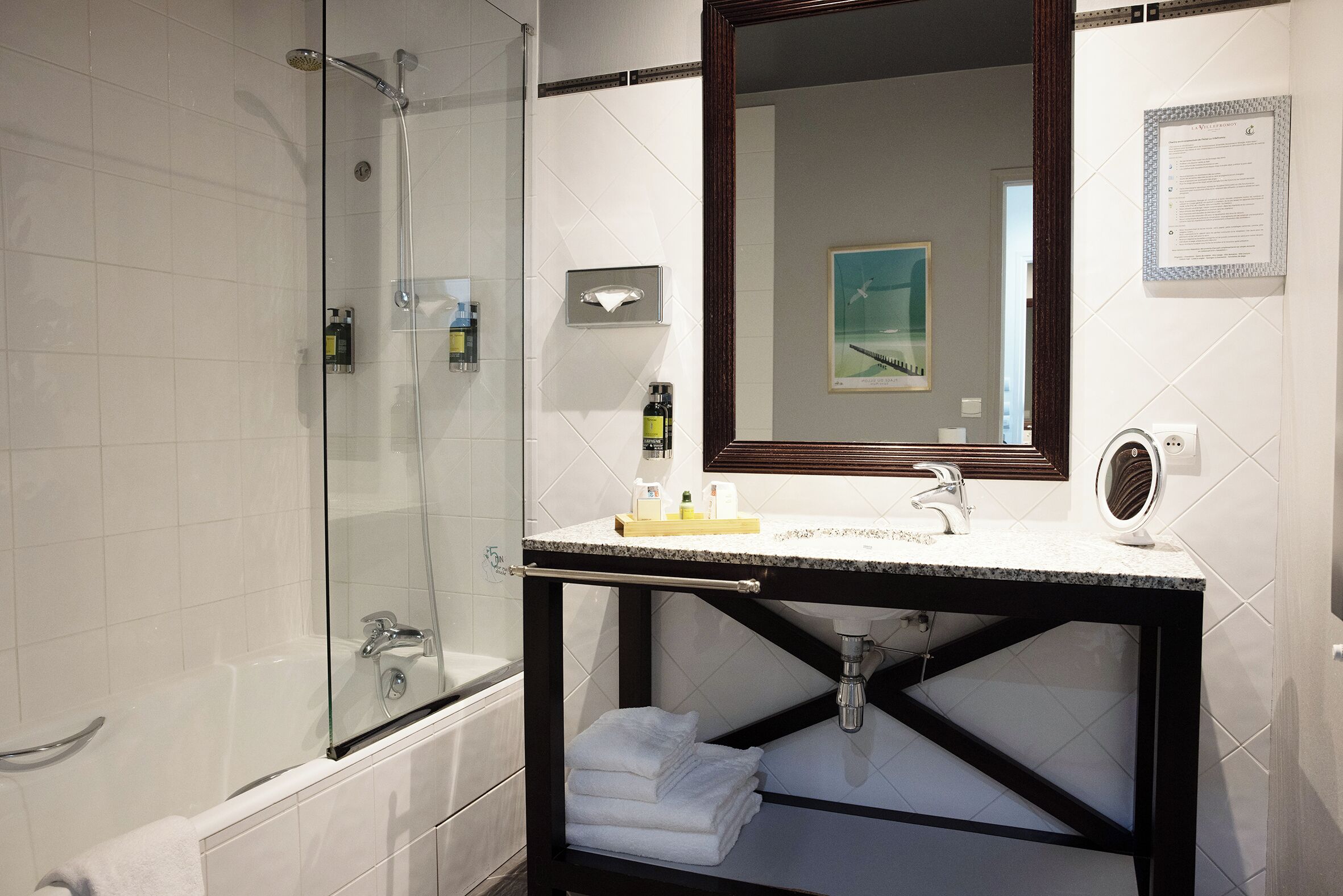 Une salle de bain moderne avec une douche à parois de verre, un meuble-lavabo avec un évier et un miroir, et des serviettes soigneusement pliées.
