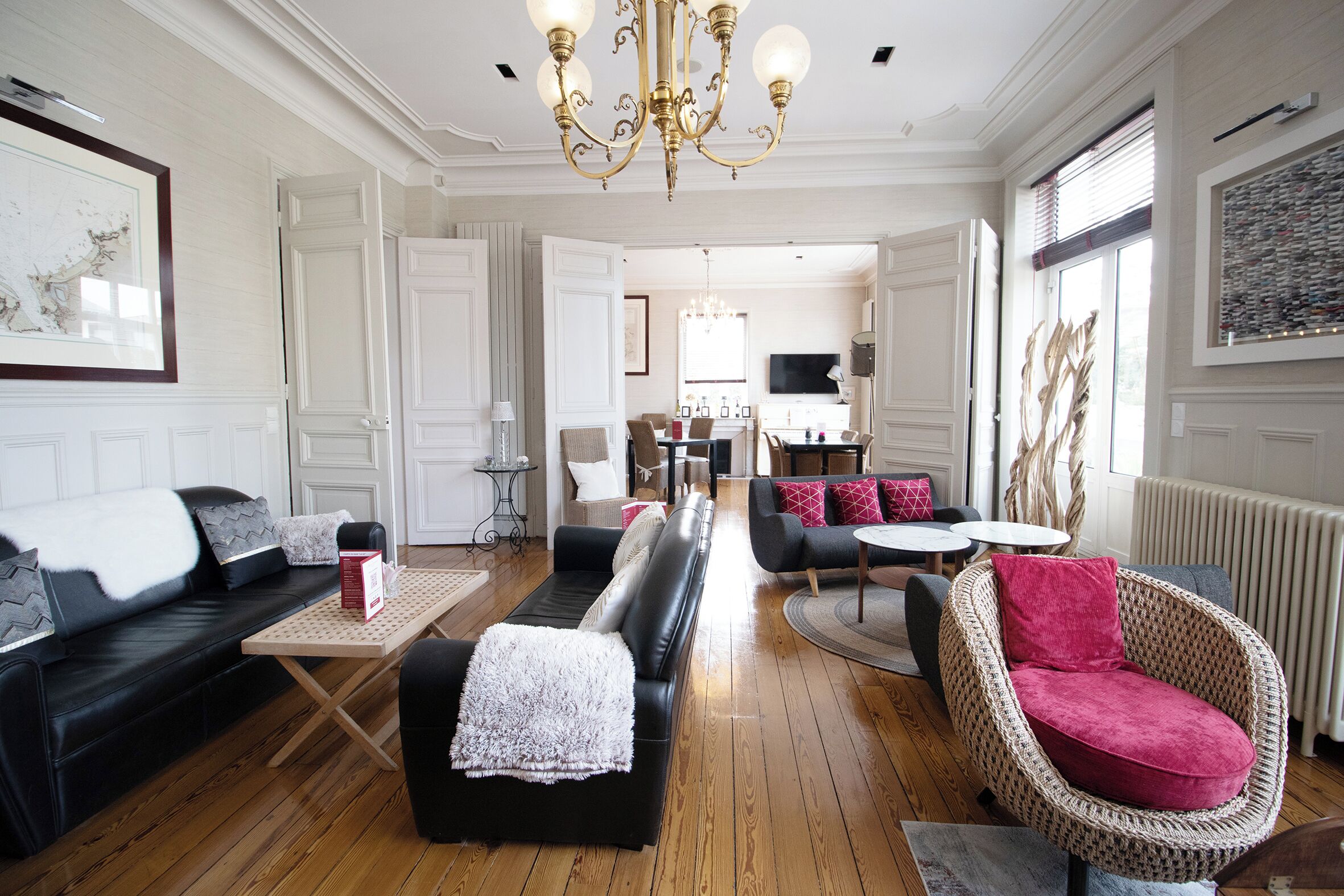 Un salon spacieux avec un canapé noir, un fauteuil en osier et, au fond, un coin repas.