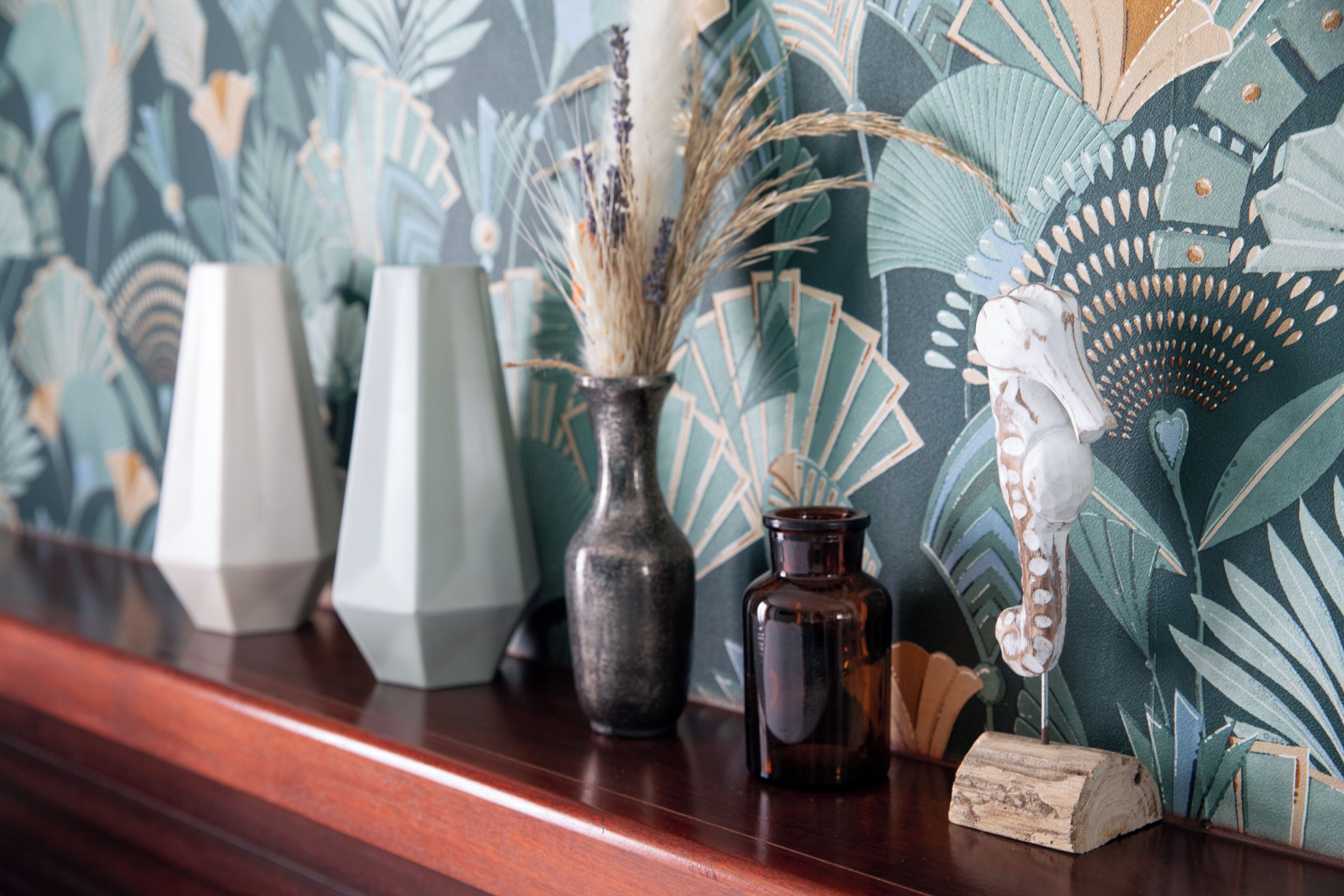 A wooden shelf with three vases and a decorative item against a patterned wall.