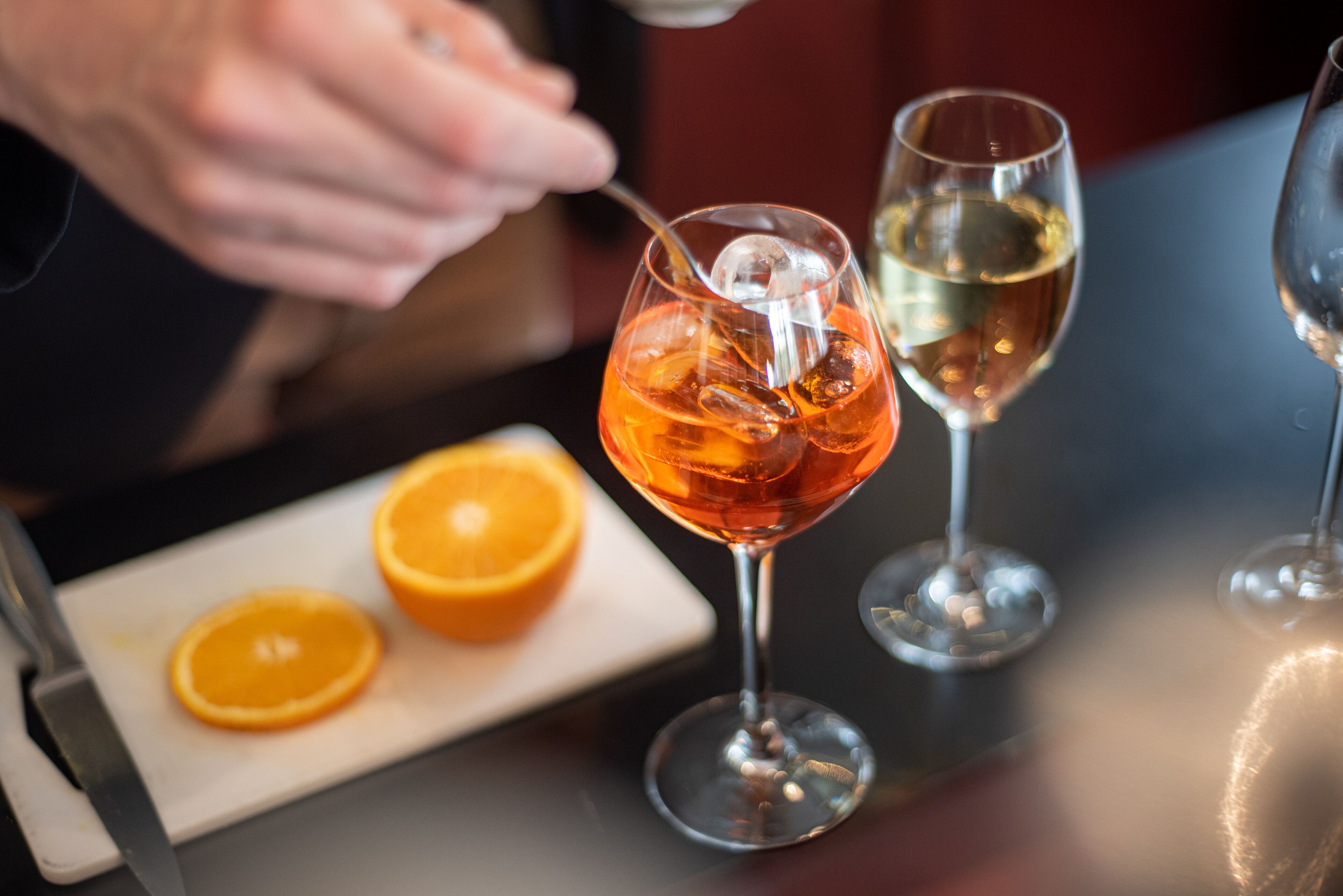 Ein Tisch mit zwei Weingläsern, eines mit rotem Getränk und das andere mit klarem Getränk, und zwei Orangenscheiben auf einem weißen Teller.