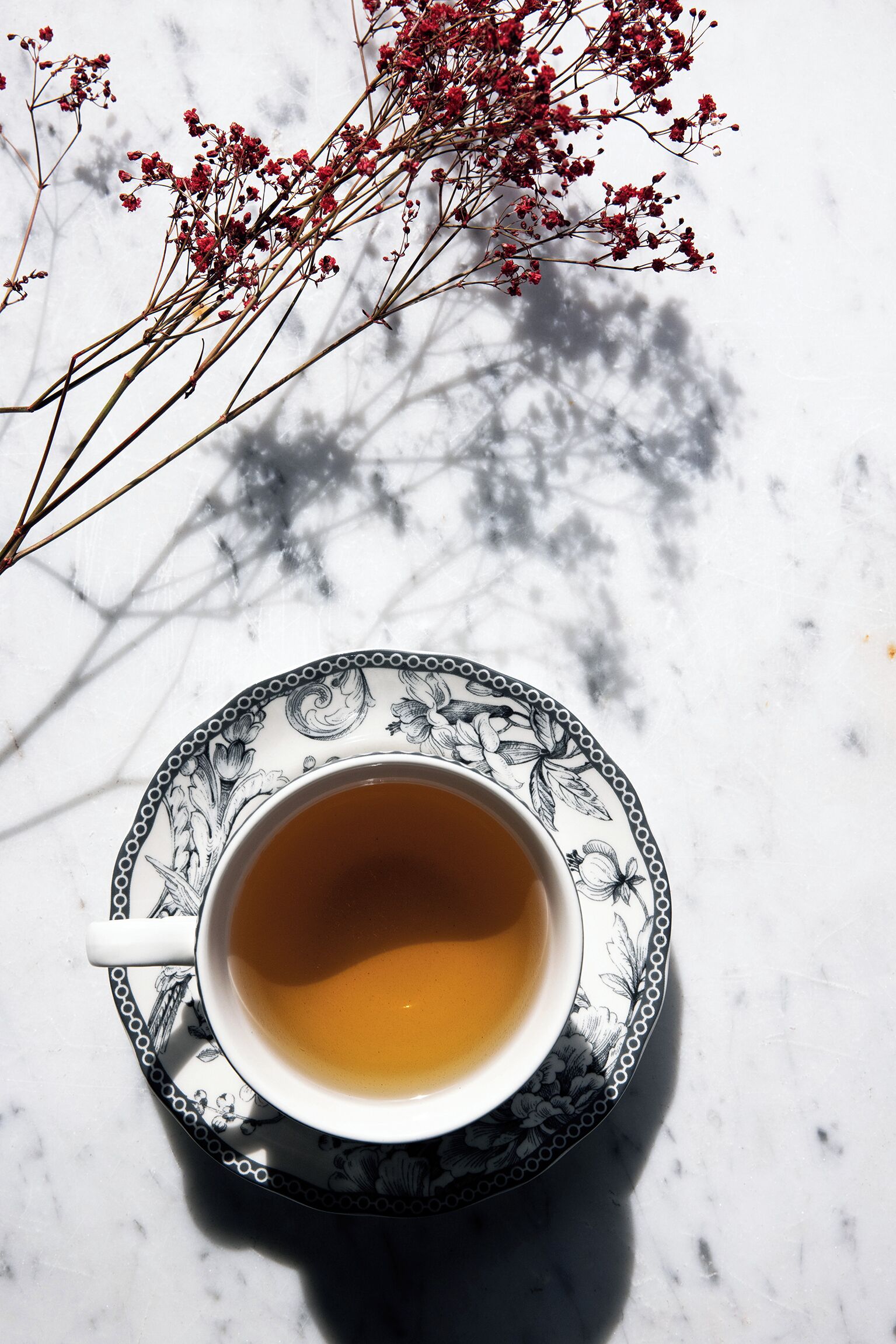 A cup of tea on a patterned saucer on a marble surface.