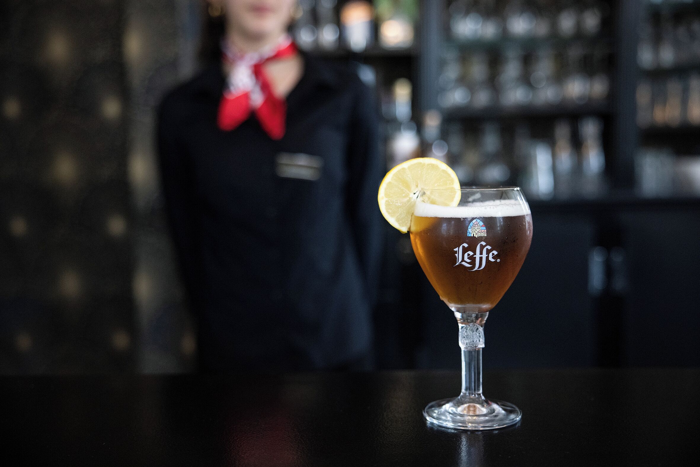 Un bar con una cerveza en la barra y un cantinero al fondo.