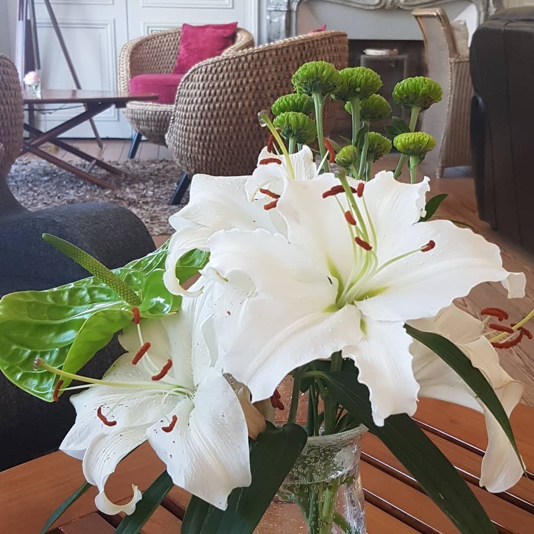 Een bloemstuk van witte lelies in een glazen vaas op een houten tafel.