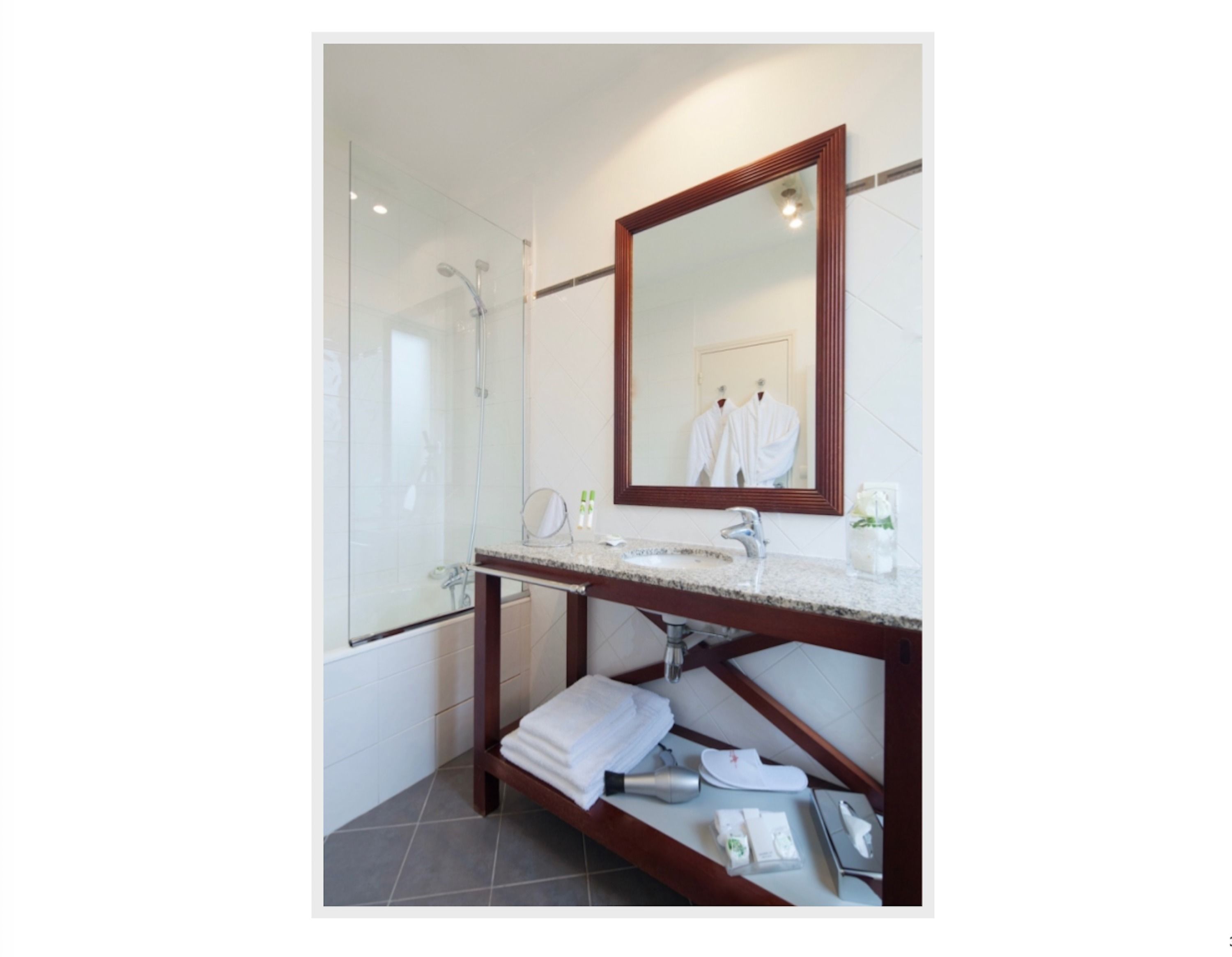 Un baño moderno con cabina de ducha de vidrio, tocador de madera con espejo y un perchero para toallas.