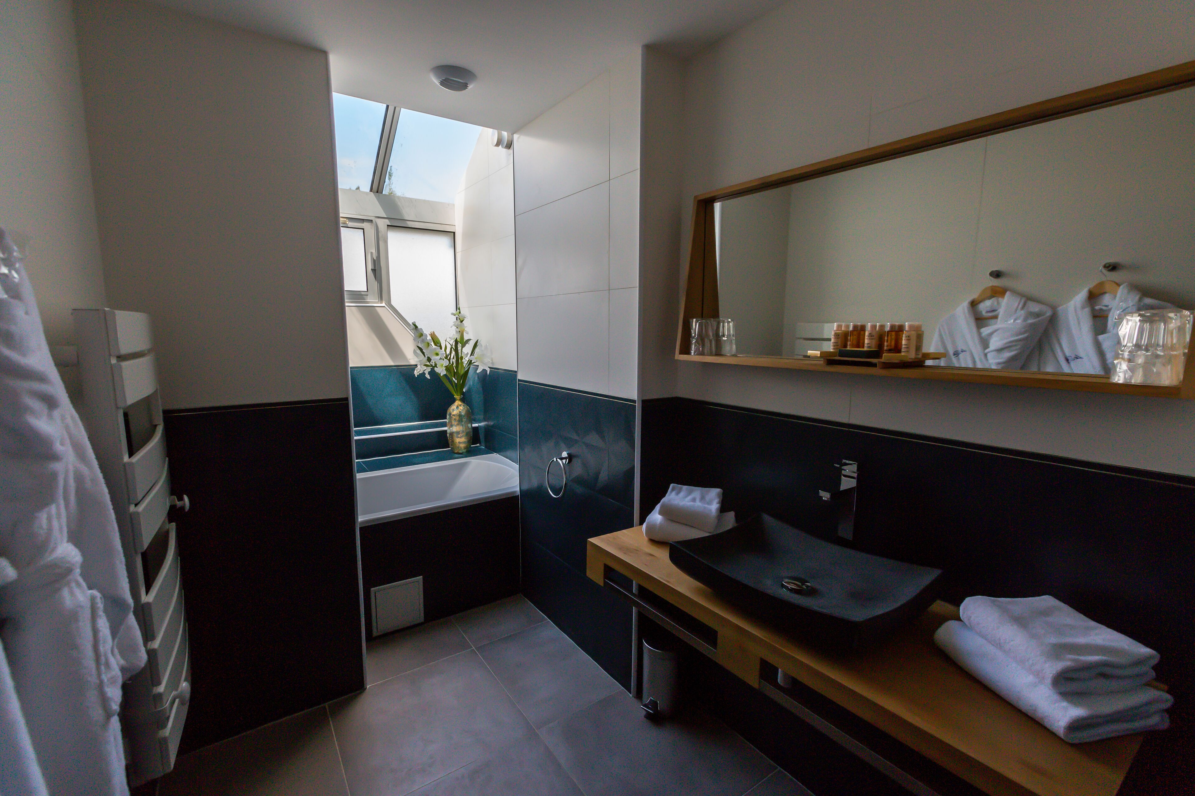 A modern bathroom with a dark vanity, a sink, and a mirror. There is a window providing natural light and a view of the sky.