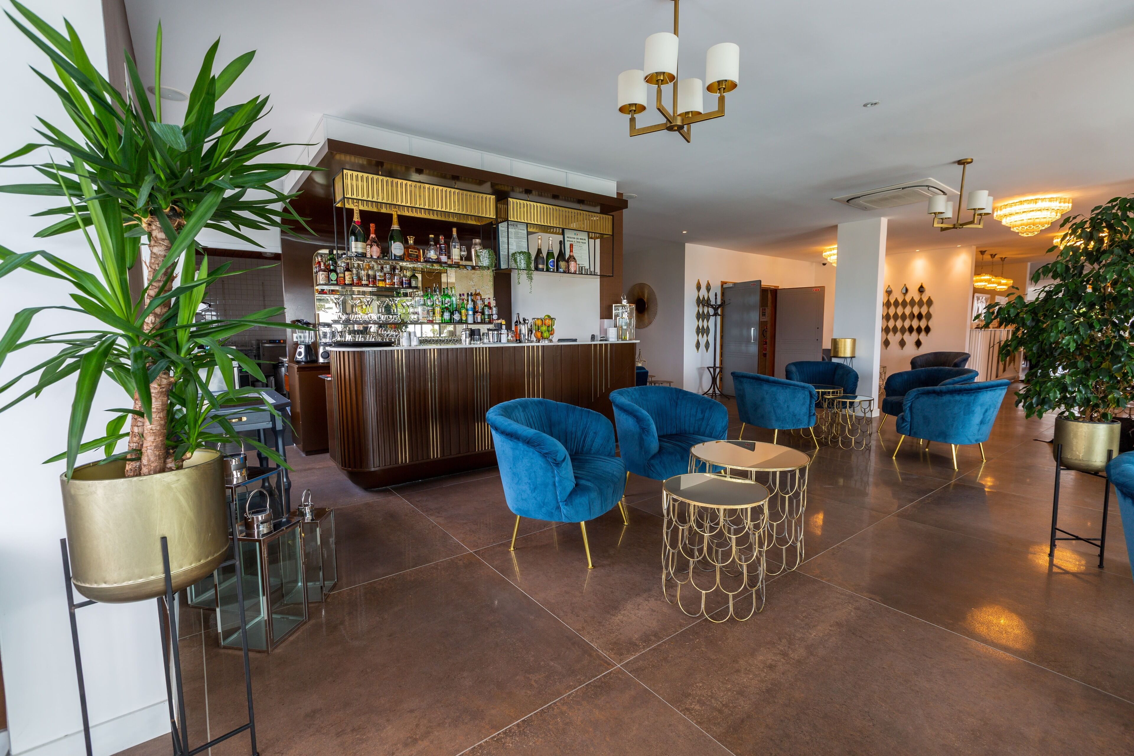 A modern bar area with a polished tile floor, blue velvet armchairs, and a well-stocked bar counter.