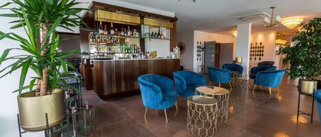 A modern bar area with a polished tile floor, blue velvet armchairs, and a well-stocked bar counter.