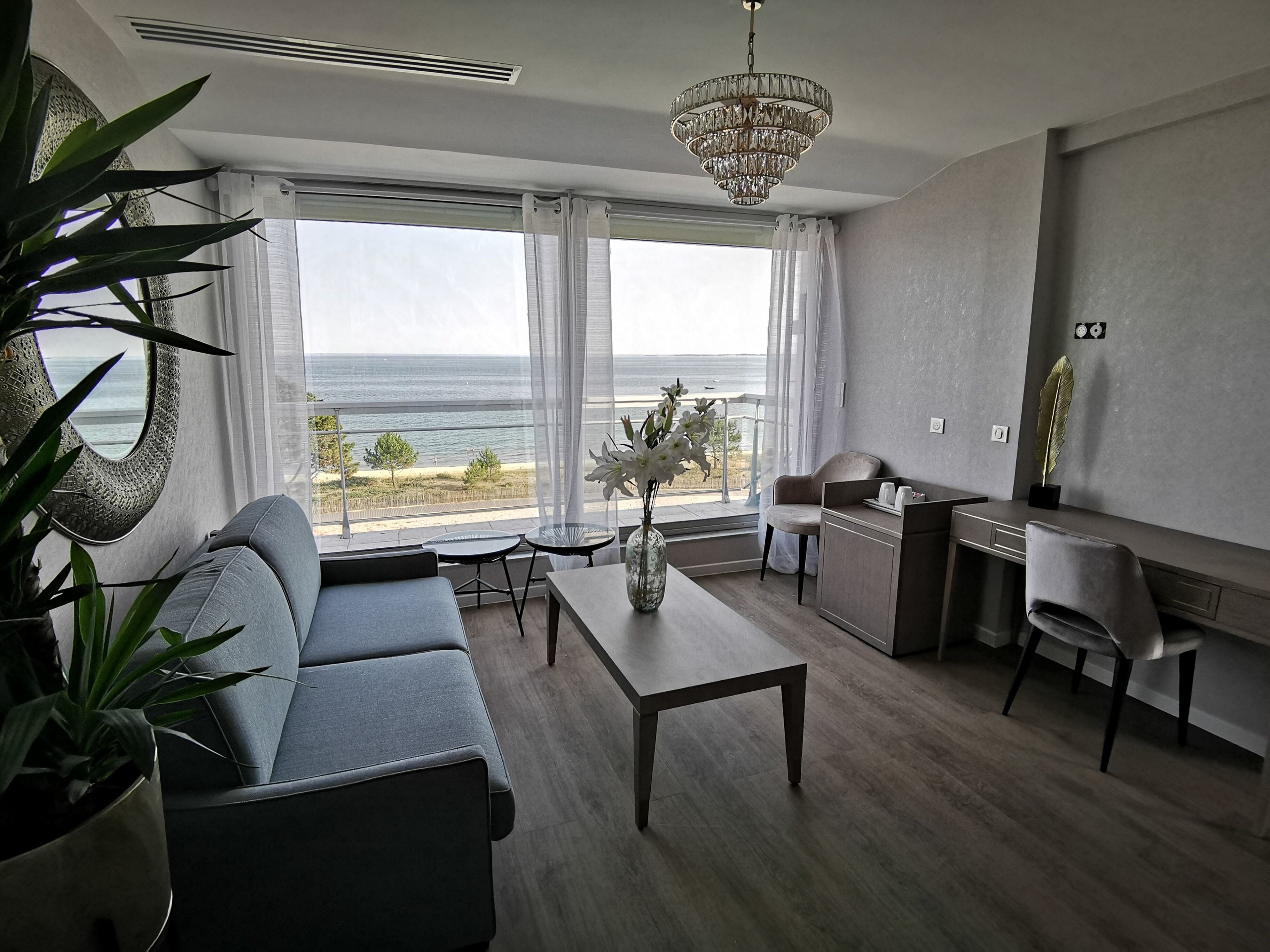 A modern living room with a view of the ocean, a chandelier, and a desk area.