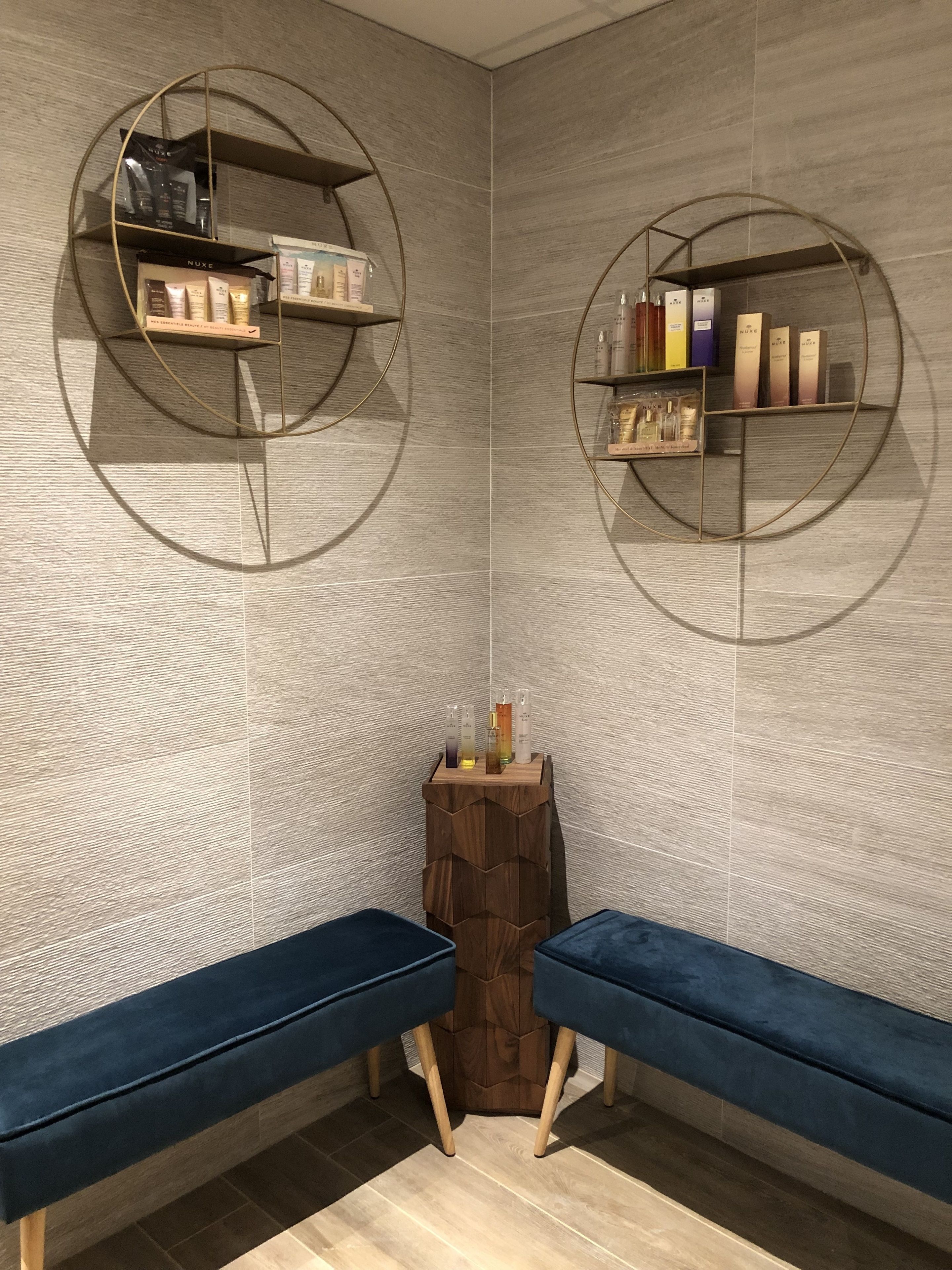 Een moderne badkamer met twee blauwe bankjes, ronde planken met toiletartikelen en een houten kruk.
