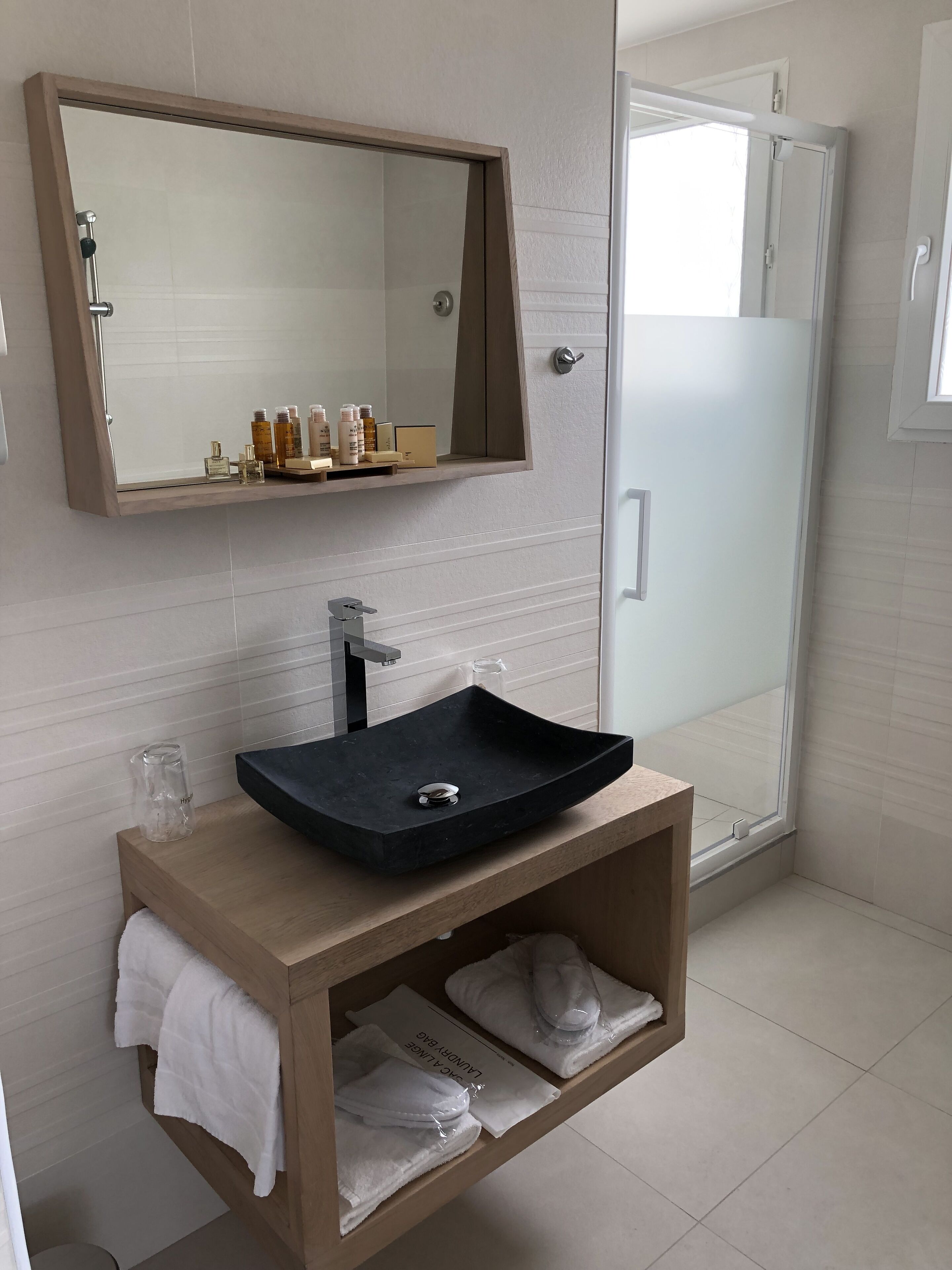 A modern bathroom with a black sink, a mirror above it, and a shower area visible through a glass door.