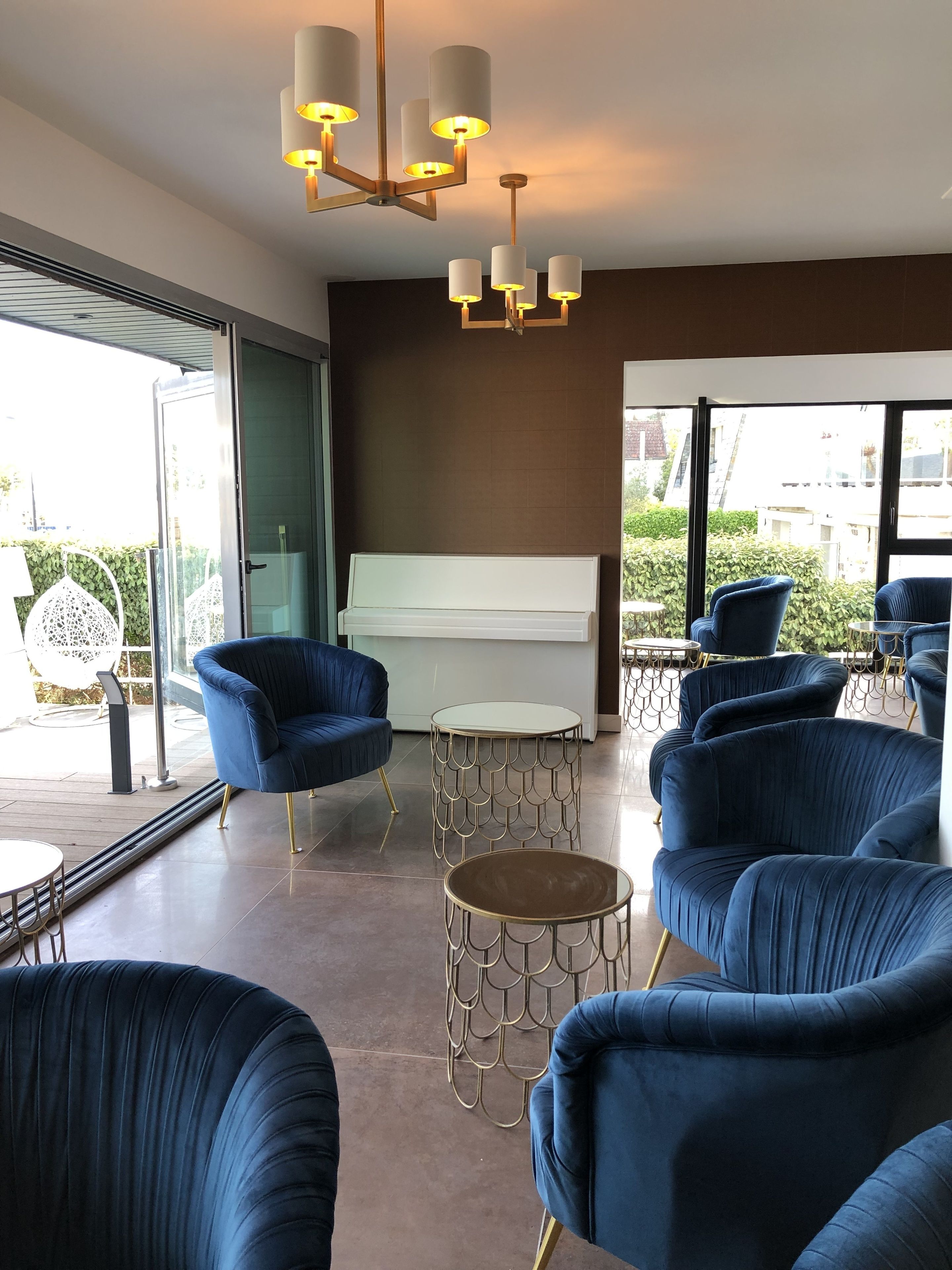 A modern lounge area with blue upholstered chairs, a central white piano, and a unique ceiling light fixture.