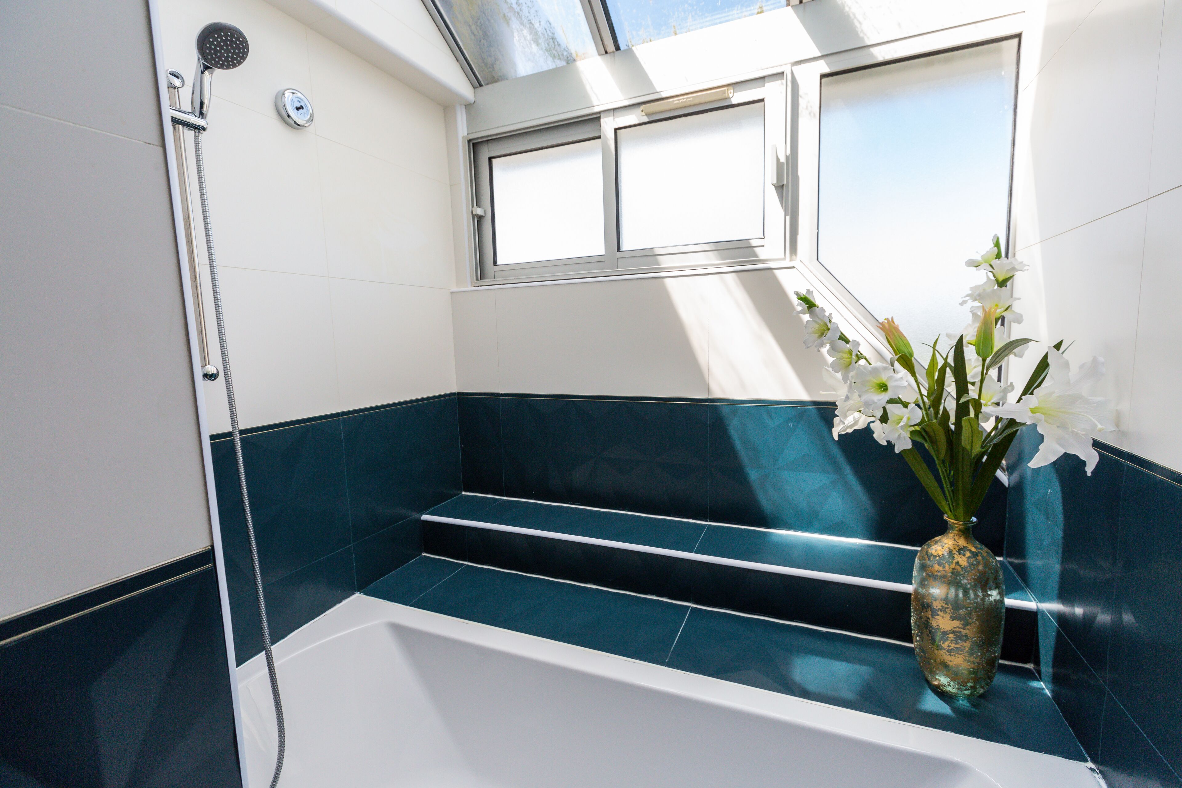 A bathroom with a shower, a window, and a vase with flowers.