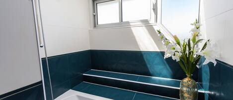 A bathroom with a shower, a window, and a vase with flowers.