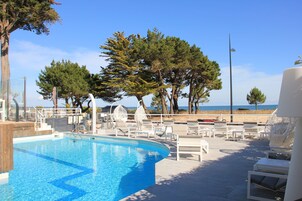 Una piscina al aire libre, sombrillas, sillones reclinables de piscina