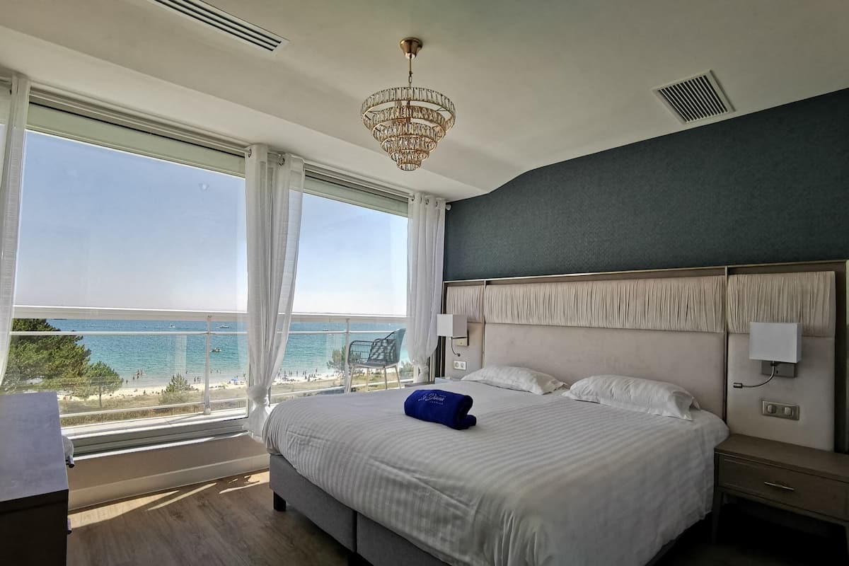 Ein Hotelzimmer mit einem großen Bett, einer Kristallleuchter, Meerblick und einem Balkon.
