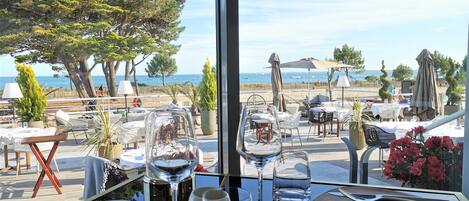 Un comedor con mesas y sillas, vista a la playa y un ventanal grande.