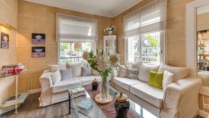 A well-lit living room with beige walls, a white sofa set, a glass coffee table, and a vase with flowers. - BRIT HOTEL CONFORT CLERIA LORIENT Centre (Lorient)