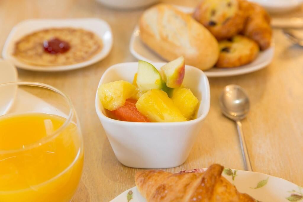 A breakfast setting with a bowl of fruit, croissants, and a glass of orange juice.