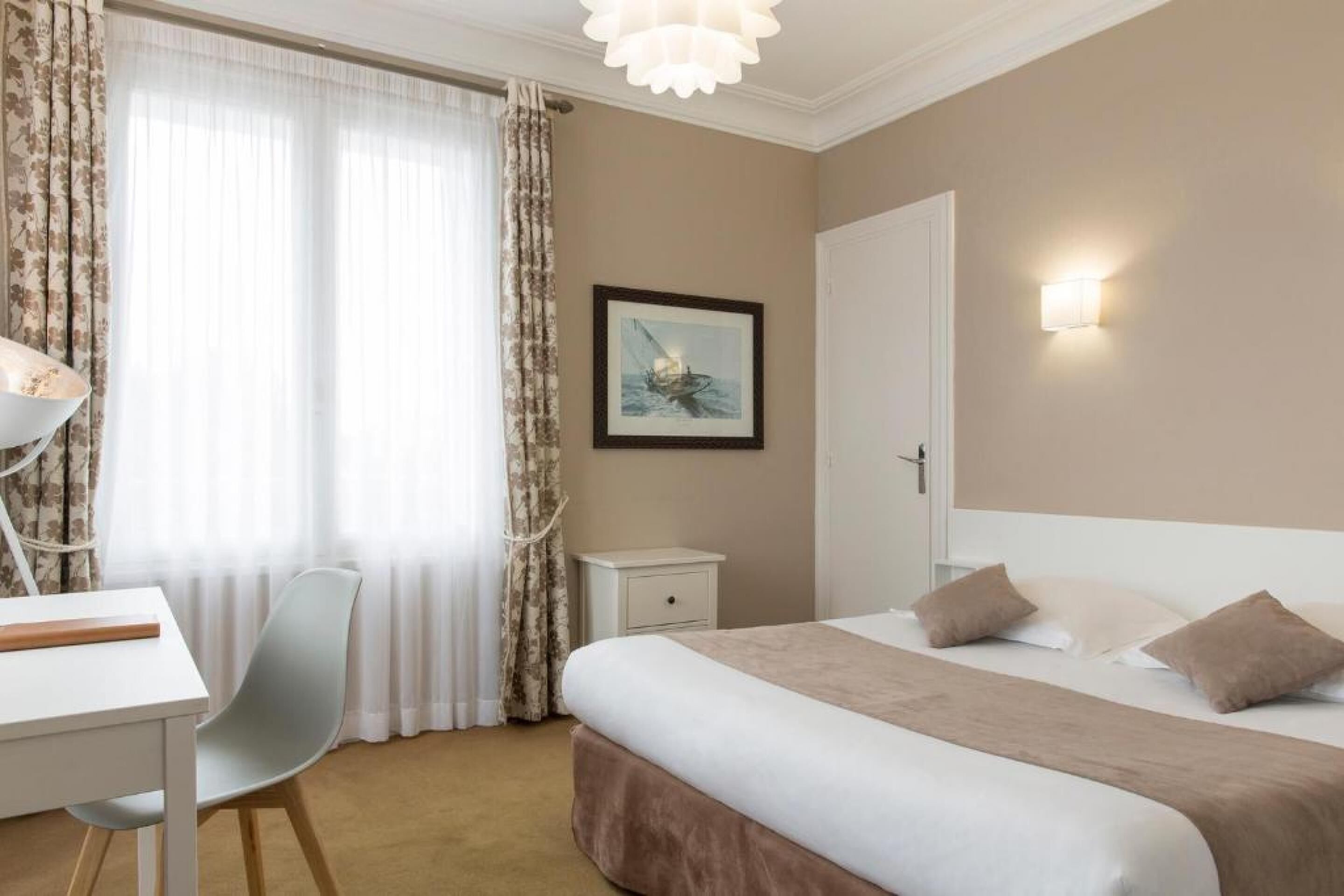 A hotel room with a bed, a desk, a chair, a nightstand, a door, and a wall-mounted picture.