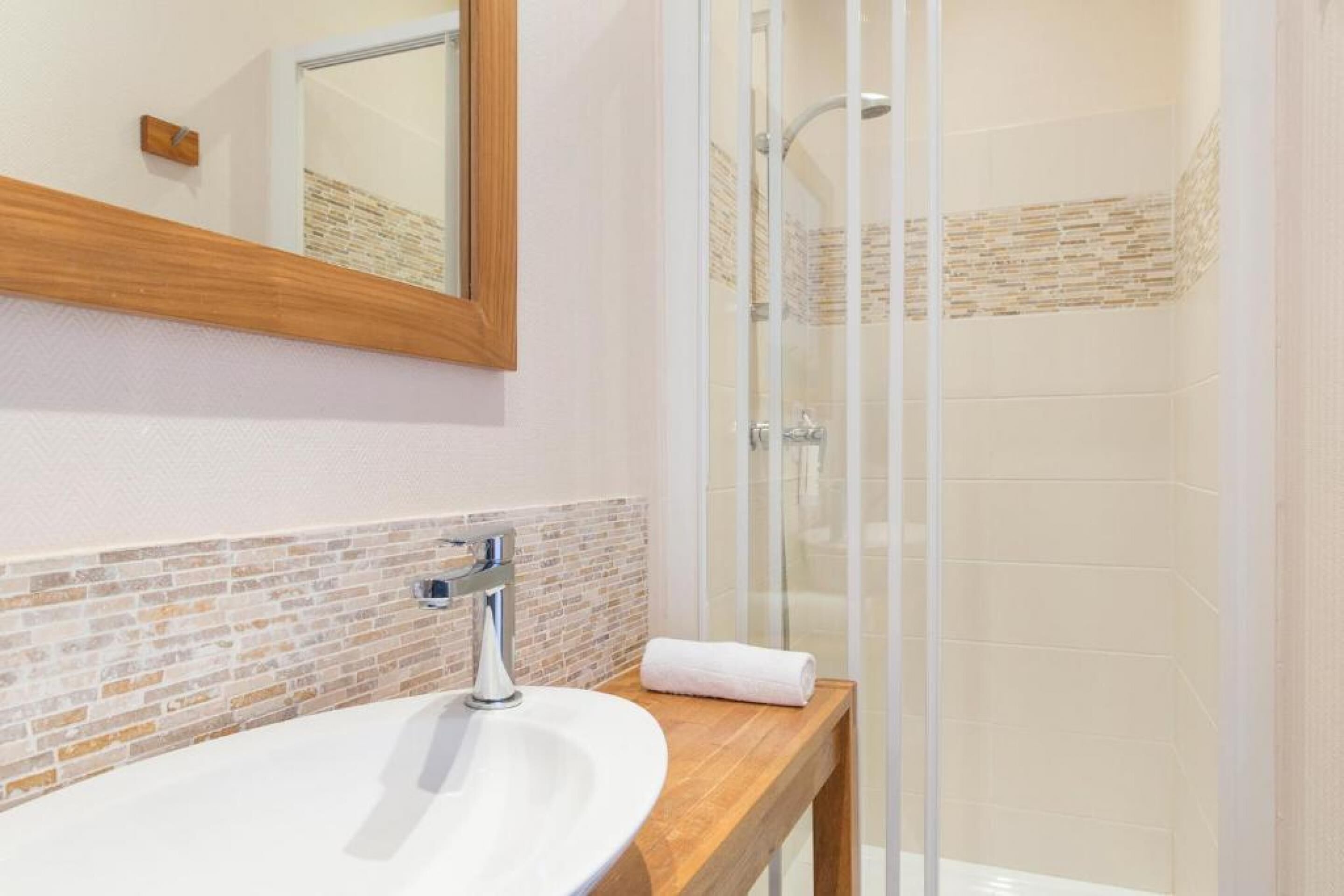 A bathroom with a wooden vanity, a white sink, a glass shower enclosure, and a mirror.