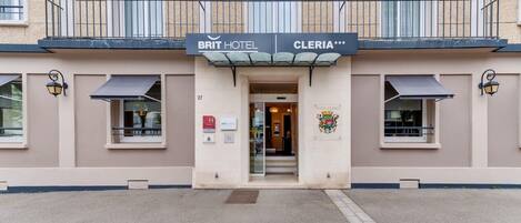 L’entrée d’un hôtel, avec une enseigne indiquant « BRIT HOTEL CLERIA » et un blason sur le mur.